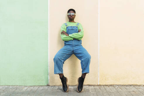 Young woman wearing smart glasses leaning on multi colored wall - PNAF05826