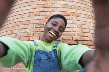 Eine fröhliche junge Frau, die ein Selbstporträt vor einer Backsteinmauer aufnimmt - PNAF05845