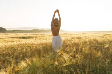 Hemdlose Frau mit erhobenen Armen inmitten einer Weizenernte im Feld stehend - AAZF00777