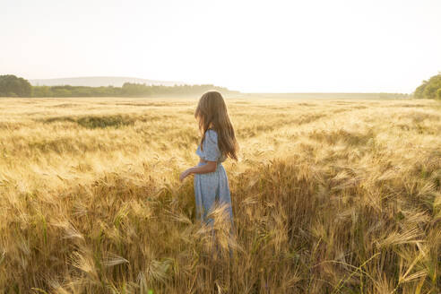 Mädchen mit langen Haaren inmitten einer Weizenernte auf einem Feld stehend - AAZF00784