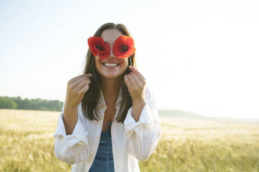 Woman holding red poppies in front of eyes at field - AAZF00843