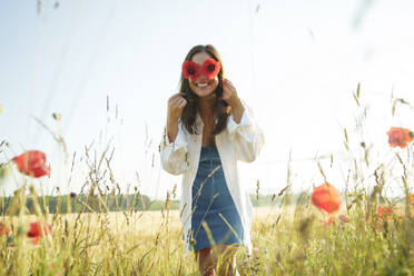 Lächelnde Frau hält rote Mohnblumen auf einem Feld vor den Augen - AAZF00845