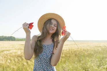Lächelndes Mädchen mit Hut hält rote Mohnblumen auf einem Feld - AAZF00847