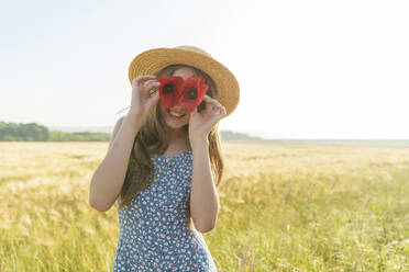 Girl holding red poppies over eyes - AAZF00848