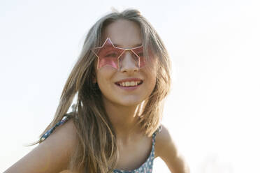 Lächelndes Mädchen mit sternförmiger Sonnenbrille vor dem Himmel - AAZF00853