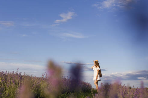 Nachdenkliche Frau steht in einem Lavendelfeld unter dem Himmel - ONAF00595