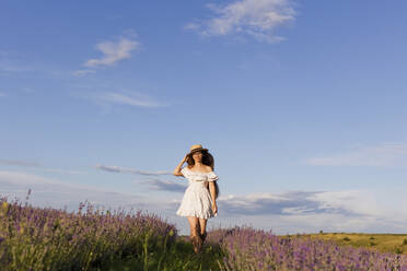 Frau in weißem Kleid geht an einem sonnigen Tag auf einem Feld spazieren - ONAF00596