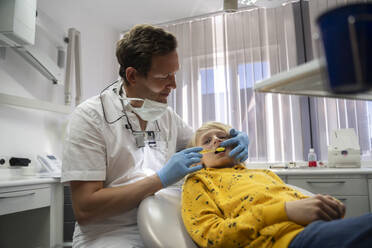 Lächelnder Zahnarzt untersucht die Zähne eines Jungen in der Klinik - NJAF00448