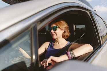 Lächelnde Frau im Auto sitzend an einem sonnigen Tag - SIF00726