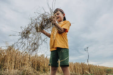 Lächelnder Junge spielt mit Heu in einem Weizenfeld - VSNF01242