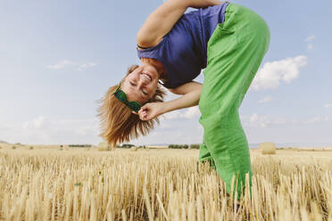 Lächelnde Frau beugt sich über ein Weizenfeld - SIF00734