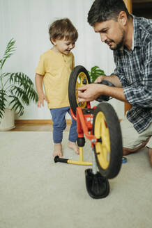 Vater repariert lächelnd das Fahrrad seines Sohnes zu Hause - ANAF01806