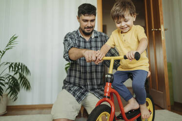 Vater hilft lächelndem Sohn, zu Hause Fahrrad zu fahren - ANAF01809