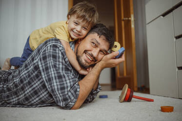 Lächelnder Vater und Sohn spielen mit Spielzeug zu Hause - ANAF01811