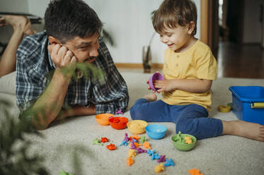 Lächelnder Vater und Sohn spielen zu Hause mit Plastikspielzeug - ANAF01813