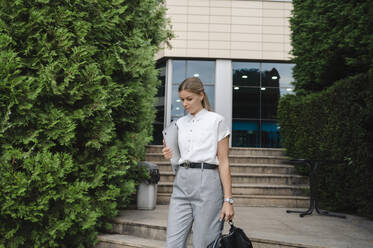 Geschäftsfrau zu Fuß mit Laptop und Tasche vor einem Gebäude - ALKF00404