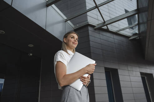 Lächelnde Geschäftsfrau mit Laptop vor einem Gebäude - ALKF00420