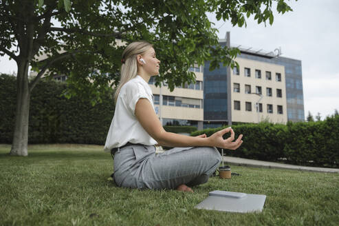 Businesswoman practicing meditation on grass in office park - ALKF00441