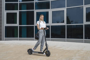 Geschäftsfrau mit Elektro-Scooter vor einem Gebäude stehend - ALKF00451