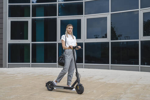 Geschäftsfrau mit Elektro-Scooter vor einem Gebäude stehend - ALKF00451