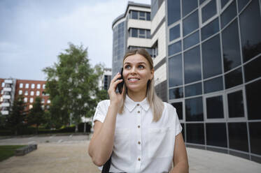 Glückliche Geschäftsfrau, die vor einem Gebäude mit ihrem Handy telefoniert - ALKF00454