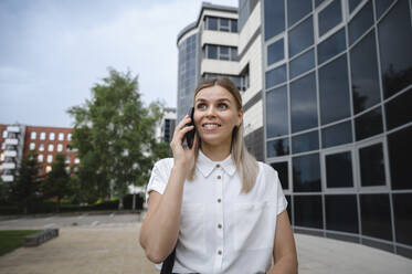 Happy businesswoman talking on mobile phone in front of building - ALKF00454