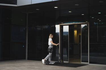 Geschäftsfrau mit Elektro-Scooter beim Betreten eines Bürogebäudes - ALKF00460