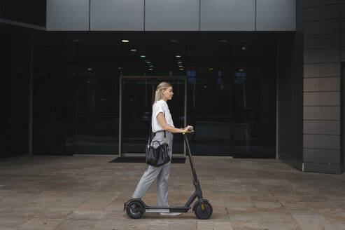 Geschäftsfrau zu Fuß mit Elektro-Scooter im Büropark - ALKF00462