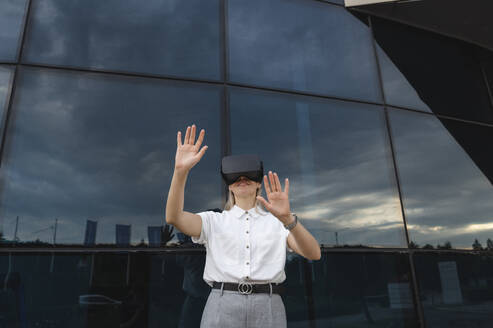 Lächelnde Geschäftsfrau gestikuliert mit Virtual-Reality-Simulator - ALKF00464
