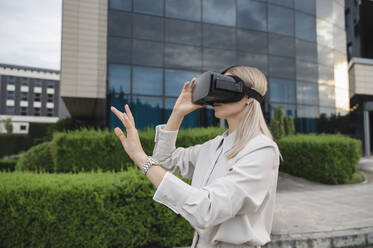 Blonde Geschäftsfrau gestikuliert mit Virtual-Reality-Simulatoren im Büropark - ALKF00480