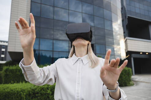 Geschäftsfrau gestikuliert mit Virtual-Reality-Simulatoren im Büropark - ALKF00481