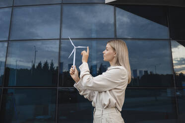 Blond businesswoman examining and touching wind turbine model - ALKF00486