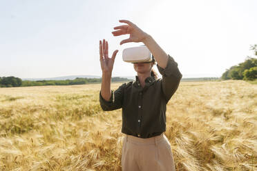 Businesswoman using virtual reality simulator and gesturing amidst barley crops - AAZF00895