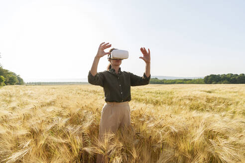 Businesswoman using virtual reality simulator standing amidst barleyt field - AAZF00896