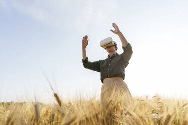 Businesswoman using wearable computer standing amidst barley crops - AAZF00899