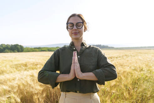 Lächelnde Geschäftsfrau beim Meditieren auf einer Weizenfarm - AAZF00903