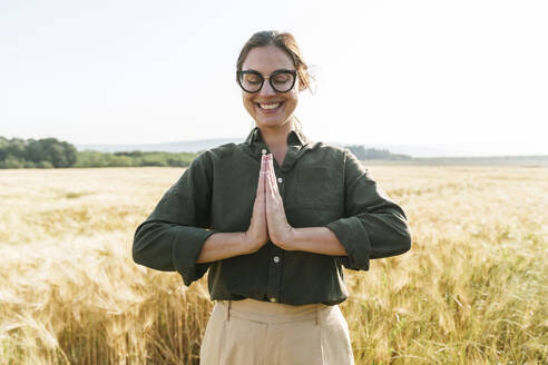 Lächelnde Geschäftsfrau beim Meditieren auf einer Weizenfarm an einem sonnigen Tag - AAZF00904