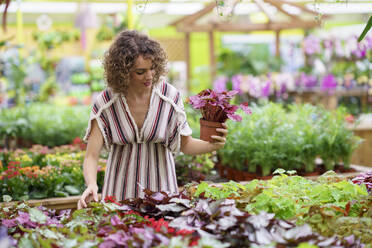 Frau, die in einer Gärtnerei stehend Pflanzen kauft - JSMF02809