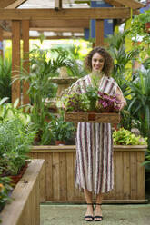 Lächelnde Frau mit einem Tablett voller Pflanzen in einer Gärtnerei - JSMF02811