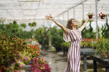 Carefree woman walking with arms outstretched in nursery - JSMF02825