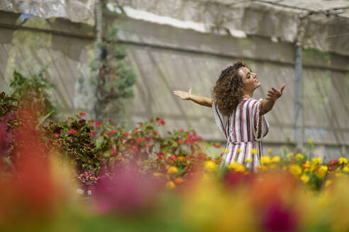 Frau genießt inmitten von Blumen in einer Gärtnerei - JSMF02827
