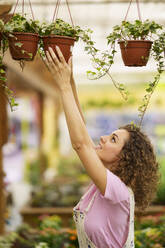 Floristin mit lockigem Haar, die Pflanzen in der Gärtnerei aufhängt - JSMF02847