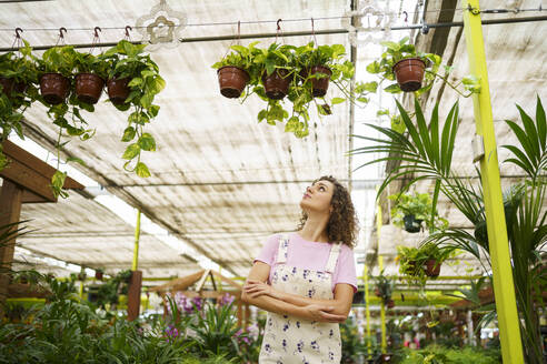Florist with arms crossed looking at plants hanging in nursery - JSMF02848