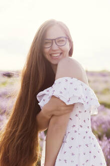 Lächelnde Frau mit langen Haaren in einem Lavendelfeld stehend - ONAF00602