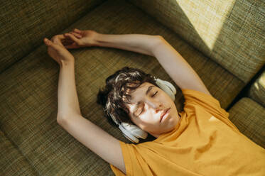 Teenage boy wearing headphones lying on sofa - ANAF01814