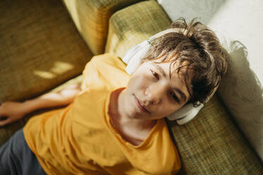 Teenage boy with headphones resting on sofa - ANAF01817