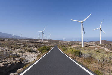 Empty road amidst wind turbines under blue sky - PNAF05853