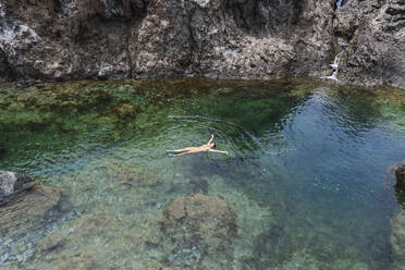 Sorglose Frau schwimmt im Meer in der Nähe von Felsen - PNAF05858