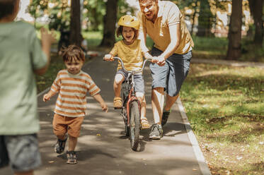 Vater hilft seinem Sohn beim Fahrradfahren auf dem Fußweg im Park - ANAF01826