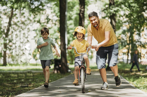 Glücklicher Vater hilft seinem Sohn beim Fahrradfahren im Park - ANAF01828